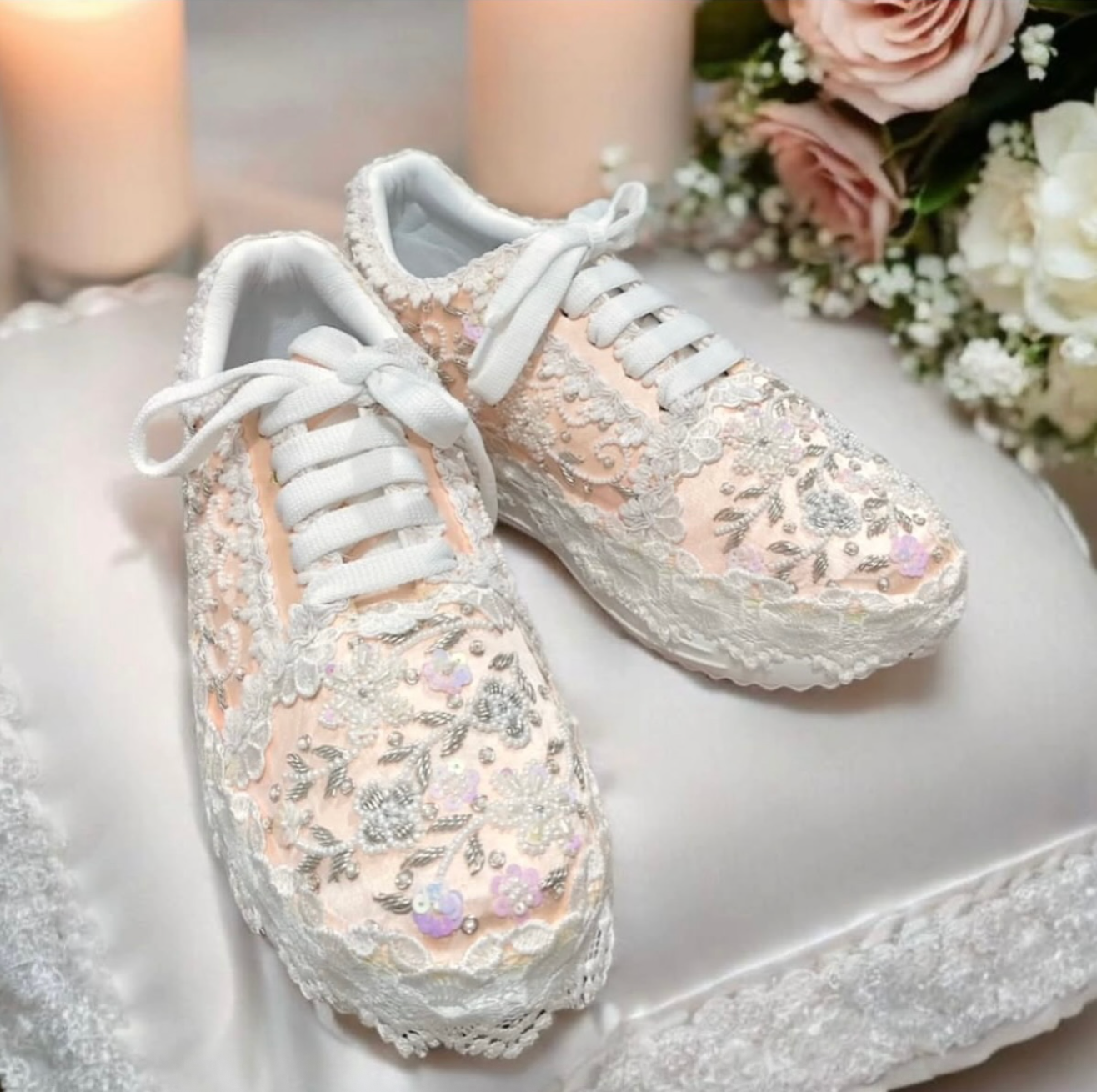 Pair of white sneakers with floral lace detailing on a white surface with flowers in the background